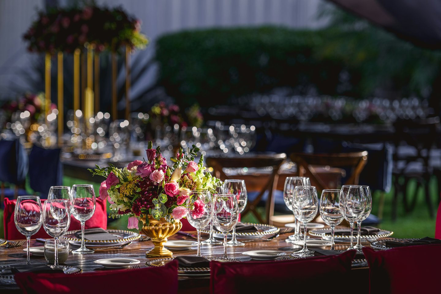 Mesa de comedor exterior puesta con centros de mesa florales y copas de vino.