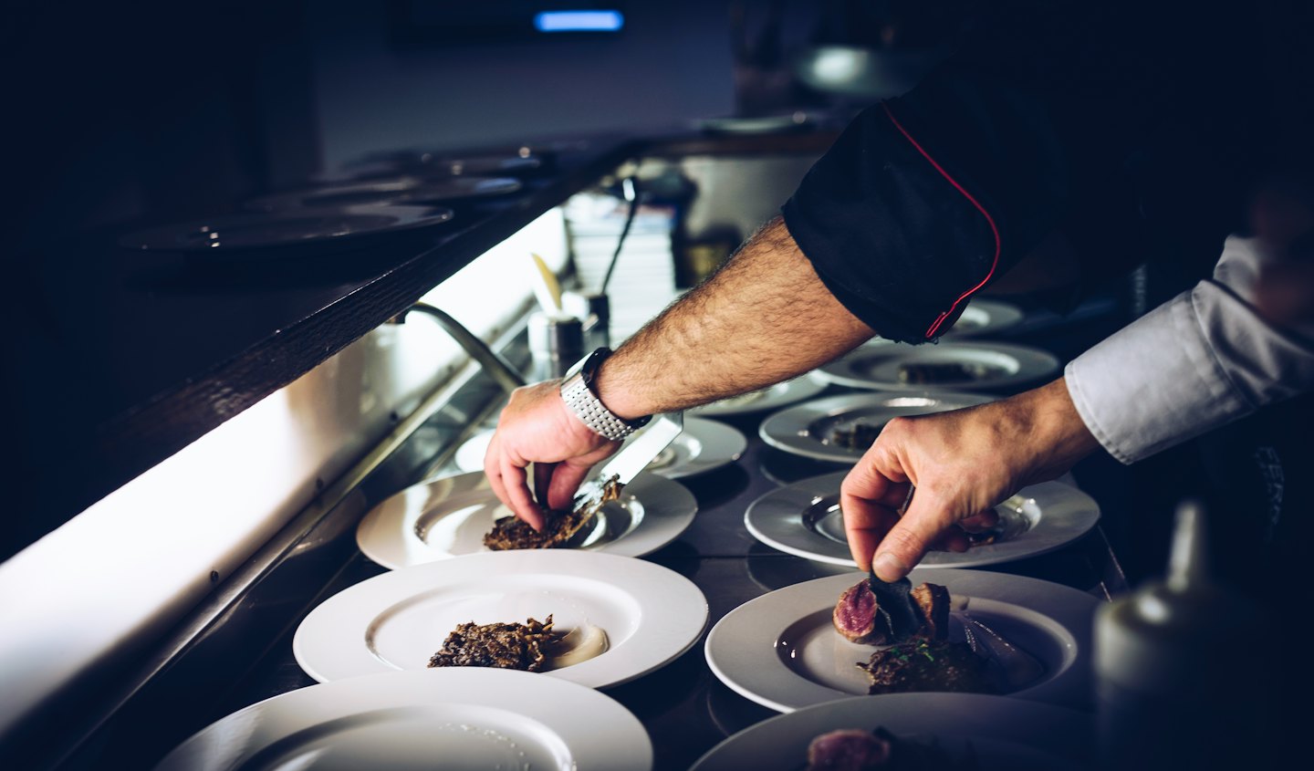 Chef emplatando meticulosamente platos gourmet en una cocina comercial.