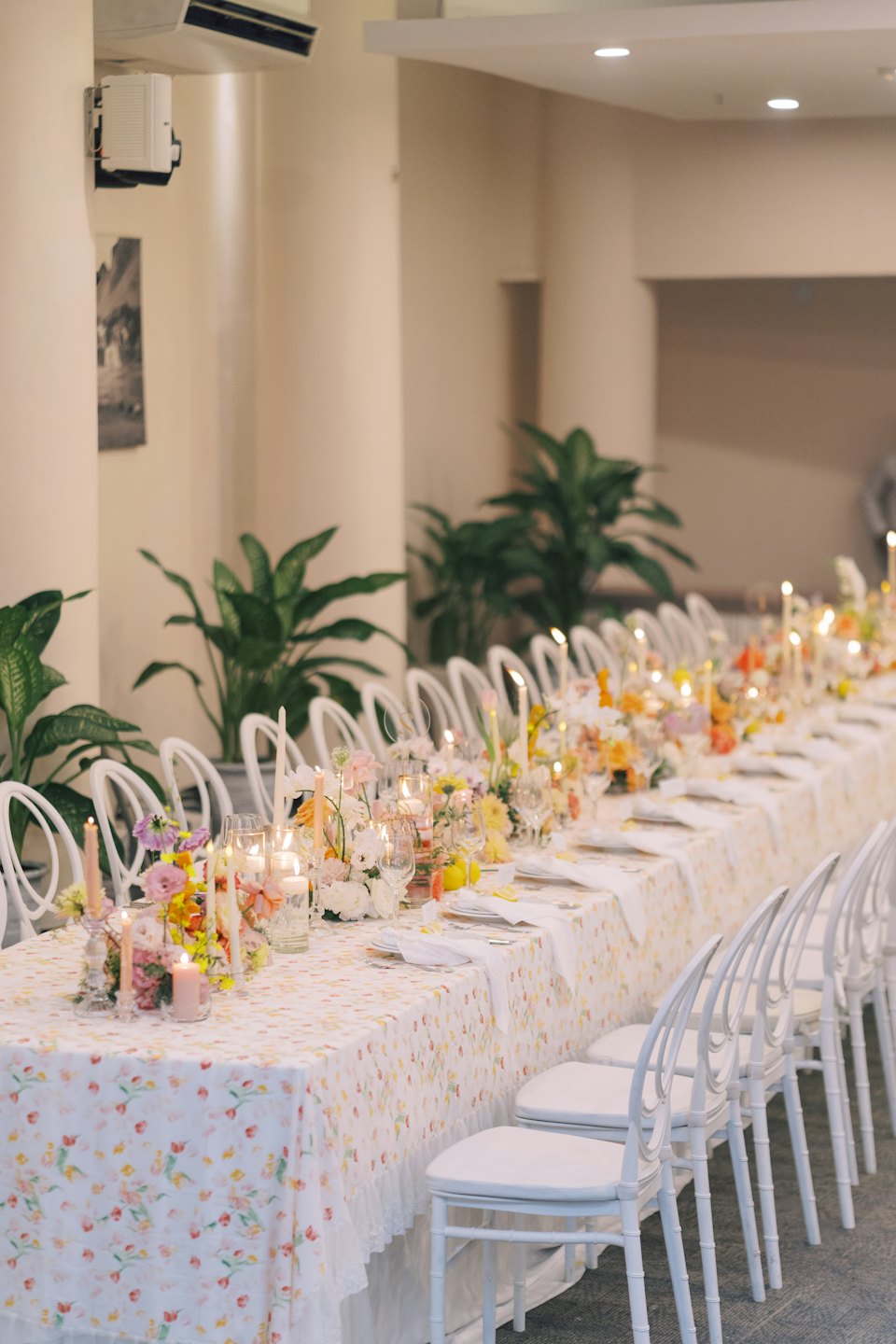 Mesa larga de banquete decorada con flores y velas.